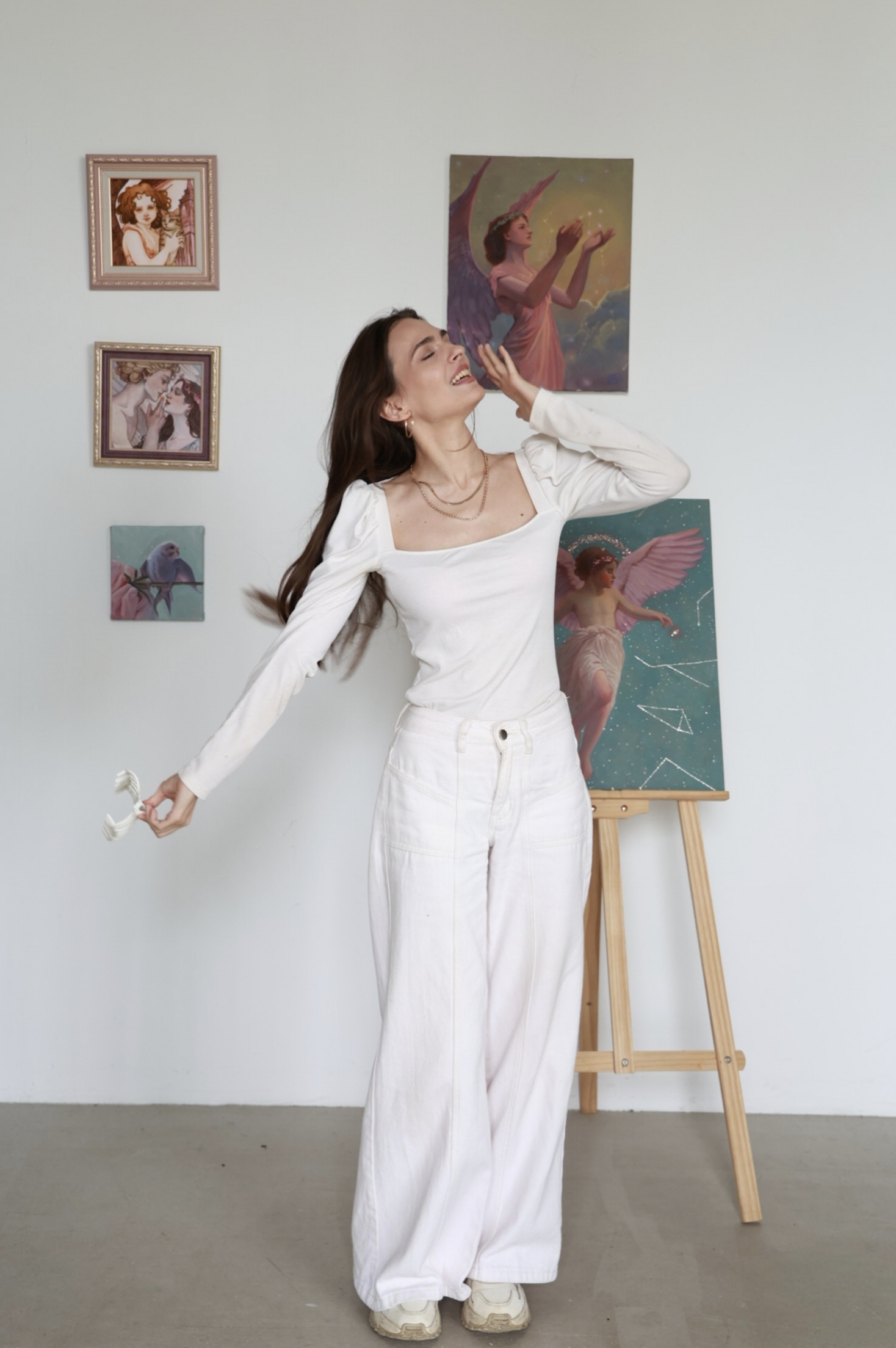 The artist in white looking upward beside her painting in the studio